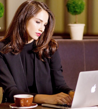 A woman sitting at a booth working on her computer with a cup of coffee